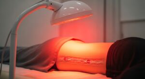 Đèn hồng ngoại đang hoạt động chiếu tia nhiệt vào vùng lưng của một người đàn ông, minh họa cơ chế nhiệt trị liệu.
